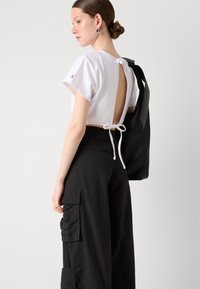 Λευκό κοντό τοπ με κοντά μανίκια, ανοιχτή πλάτη δεμένη με λευκές κορδέλες; συνδυασμένο με μαύρο cargo παντελόνι που διαθέτει πολλές τσέπες.