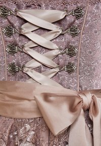 Laced korsett med satinband i mjuk rosa, med utsmyckade metallstängningar och ett texturerat blommönster, åtföljd av en matchande satinsløjfe.