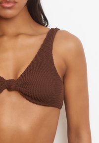 Top bikini marrone con texture, spalline spesse e un dettaglio a fiocco al centro, con una forma triangolare per una migliore copertura.