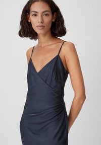 Navyblauwe satijnen jurk met dunne spaghettibandjes, V-hals en geplooide zijdetails voor extra textuur. Strakke, aansluitende silhouet.