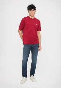 Punainen lyhythihainen paita, jossa on tekstuuri ja pyöreä pääntie, yhdistetty sinisiin farkkuihin ja valkoisiin lenkkareihin.