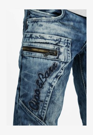 Denim jeans met een blauwe, vervaagde wassing. Kenmerken zijn onder andere een ritszak en decoratieve stiksels. Gelaagd stof met een versleten uiterlijk.