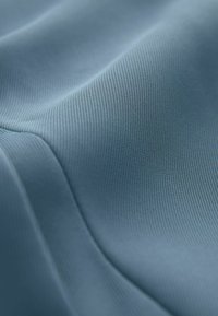 Zbliżenie na miękką, gładką niebieską tkaninę o drobnej prążkowanej fakturze i delikatnych fałdach tworzących zakrzywione cienie i refleksy.