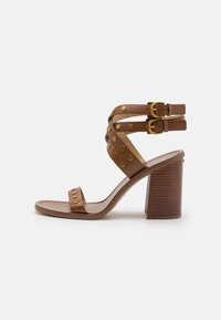 Brune lær sandaler med hæl og guld-nitter, to ankelremme med spænder og en tekstureret træklods hæl. Glat sål med minimal polstring.