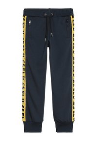 Marina joggerbyxor tillverkade av mjukt tyg, med sidofickor med dragkedja och gula midjeaxlar med ett upprepat textmönster.