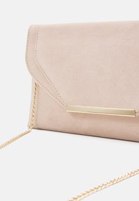 Beżowa torebka kopertowa z teksturowanym, imitującym zamsz wykończeniem, wyposażona w złoty metalowy akcent i łańcuszkowy pasek. Zapięcie w stylu koperty.