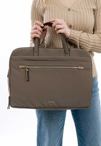 Brown padded tote bag with dual top handles, front zip pocket, and subtle branding. Features a smooth texture and sturdy zippers.
