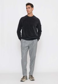 Maglione grigio scuro lavorato a maglia con scollo rotondo e dettagli a coste sulle spalle, abbinato a pantaloni plissettati grigio chiaro e sneakers beige.