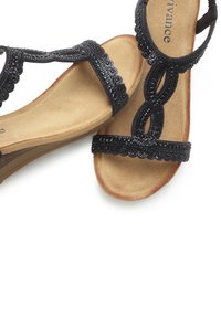 Black strappy sandals with decorative beading, soft beige footbed, and scalloped accents on straps, featuring a low-profile sole.
