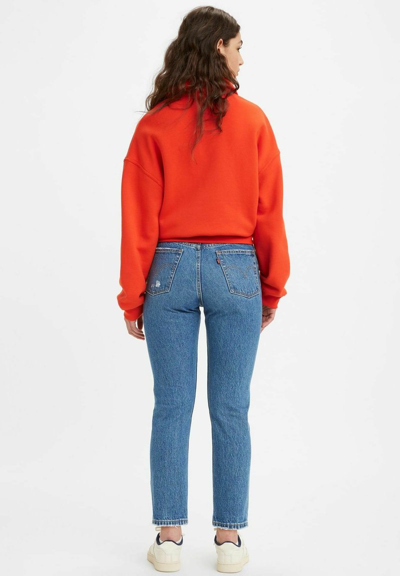 Felpa rossa oversize, jeans blu a vita alta con tasche posteriori e sneaker color crema. Tessuto morbido e vestibilità casual con silhouette rilassata.