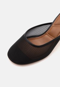 Ballerine plate en mesh noir avec embout carré et semelle intérieure marron matelassée sur fond blanc.
