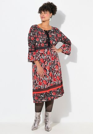 Floral print jurk met zwarte achtergrond, rode en witte bloemen. Belmouwen, knielang met een zwarte strikdetail en bijpassende tailleband. Zilveren enkellaarsjes.