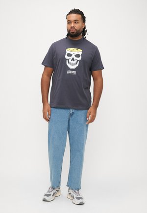 T-shirt cinzenta de manga curta com gráfico de caveira e halo amarelo, combinada com jeans azul claro de perna reta e ténis cinzentos.