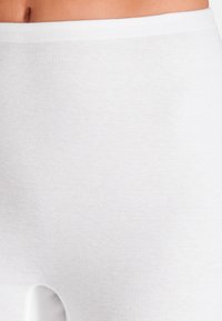 White ribbed leggings made of soft material. They feature an elastic waistband and a smooth texture, designed for comfort and ease of wear.