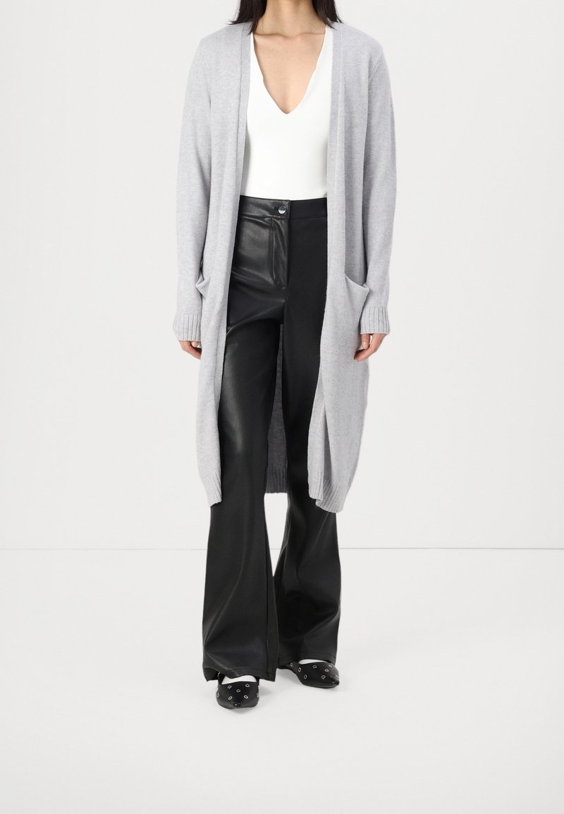 Grå lång kofta i mjukt stickat material, med öppen framsida, ribbade muddar och sidofickor, som matchas med figurnära svarta faux läder byxor.