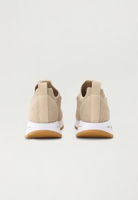Pair of beige knitted slip-on sneakers with white midsoles and gum rubber outsoles, shown from the back on a plain background.