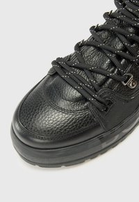 Baskets noires avec un dessus en cuir texturé, un bout rond prononcé, des œillets renforcés et des lacets noirs avec des coutures blanches contrastées.