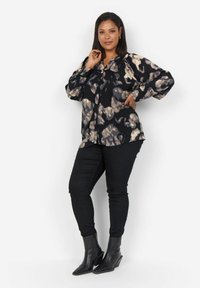 Blusa nera con motivo astratto beige chiaro, maniche lunghe, chiusura a bottoni, abbinata a pantaloni neri attillati e stivaletti con tacco a punta neri.