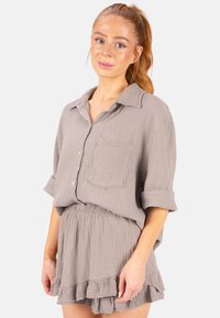 Ensemble en deux pièces gris clair et texturé comprenant une chemise à boutons avec une poche poitrine et une jupe à volants avec taille élastique.