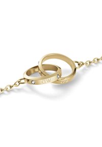 Auksinis apyrankė su dviem persipynusiais žiedais, vienas iš jų graviruotas "MD" ir papuoštas mažuoju kristalu. Lygus, poliruotas paviršius.