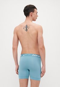 Lyseblå Nike boxer shorts med tætsiddende pasform, der har en bred, mærket talje og et glat, strækbart materiale. Ingen synlige mønstre.