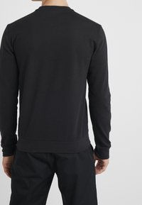 Felpa nera a maniche lunghe con colletto a girocollo, polsini e fondo a coste. Design semplice e solido senza motivi o decorazioni.
