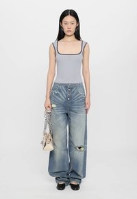 Grå ærmeløs bodysuit, højtaljede distressed blå jeans med store lommer, og en skinnende sølvfarvet taske med kædestrop. Sorte sko.