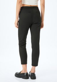 Svarta slim-fit byxor med en slät textur, med en bred midjeband och två bakfickor, parat med svarta loafers.