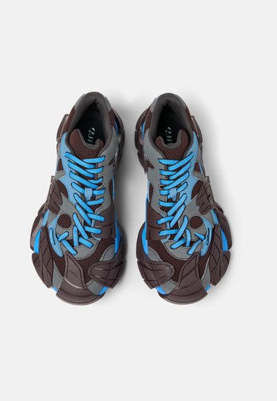 Bruna och grå mesh-sneakers med blå snören och detaljer, samt en texturerad gummisulor. Distinkt oregelbunden form och design detaljer.