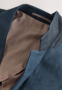 Blaues Leinenblazer mit einem glatten, gemusterten braunen Futter, ausgestattet mit einem maßgeschneiderten Kragen und sorgfältigen Nähten entlang der Kanten.