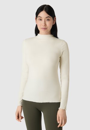 Langærmet elfenben ribbet top med høj krave samt bølget kant og manchetter. Kombineret med olivengrønne leggings med tætsiddende design.