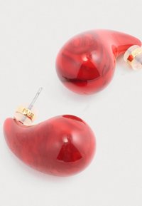 Czerwone słuchawki douszne o błyszczącym, marmurowym wykończeniu, z ergonomicznym kształtem, złotymi akcentami i przezroczystymi silikonowymi końcówkami.