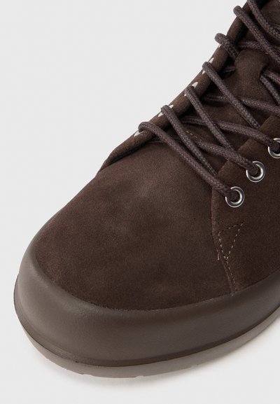 Pantofii de drumeție din suede maro au un vârf rotund, o talpă din cauciuc rezistent, ochiuri metalice și șireturi plate. Partea superioară texturată oferă aderență și suport.