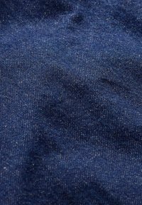 Tmavě modrá džínová tkanina s hladkým povrchem a jemným vzorem, se slabými variacemi v barvě a jemnými detaily šití.