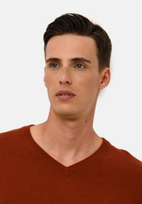 Maglione a maglia color ruggine con scollatura a V, caratterizzato da una trama morbida e una vestibilità aderente attorno alle spalle e al collo.