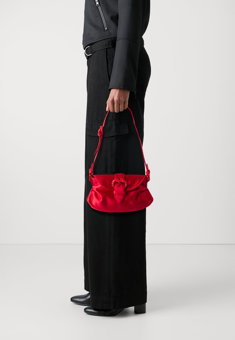Red satin handbag with a rounded shape, featuring a twist lock closure and a short handle. Worn with black casual pants and shoes.