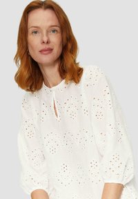 Witte blouse met broderie anglaise details, een ronde halslijn met een keyhole-uitsnijding, en opgeblazen mouwen.