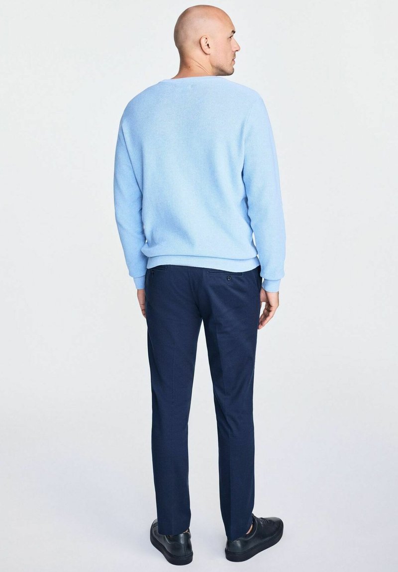 Hellblaues Sweatshirt, runder Ausschnitt, gerippte Textur. Kombiniert mit navyblauen Slim-Fit-Hosen. Schwarze Sneaker runden das Outfit ab. Ansicht von hinten.