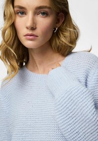 Pull en maille bleu clair avec poignets côtelés et coupe décontractée. Texture douce, avec un col rond et des manches légèrement surdimensionnées.