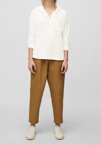 Sudadera blanca de mangas largas con un bolsillo frontal y cordones, combinada con pantalones de pierna ancha beige y zapatillas color crema. Un conjunto simple y casual.