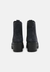Bottes cheville en daim noir avec un talon large et épais, une languette de traction à l'arrière, et une texture lisse. Conception élégante avec des détails de couture minimalistes.