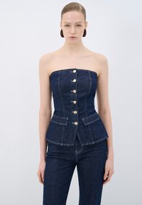 Top senza spalline in denim scuro con un design aderente, caratterizzato da bottoni frontali e due tasche anteriori. Tessuto testurizzato e vita strutturata con peplum.
