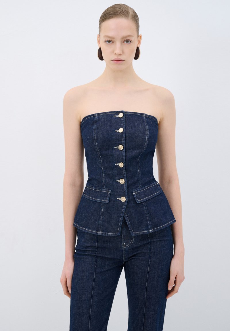 Top senza spalline in denim scuro con un design aderente, caratterizzato da bottoni frontali e due tasche anteriori. Tessuto testurizzato e vita strutturata con peplum.