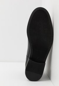 Černá kožená bota s texturovanou gumovou podrážkou a vzorovaným profilem pro lepší přilnavost. Design je elegantní s kulatou špičkou.