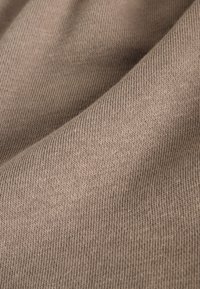 Gros plan d’un tissu tricoté beige doux avec une texture côtelée fine et uniforme et des plis doux.