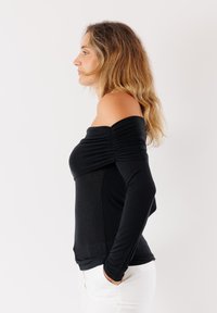 Top nero con spalle scoperte e maniche lunghe, caratterizzato da tessuto arricciato all'collo. Materiale morbido e design aderente.