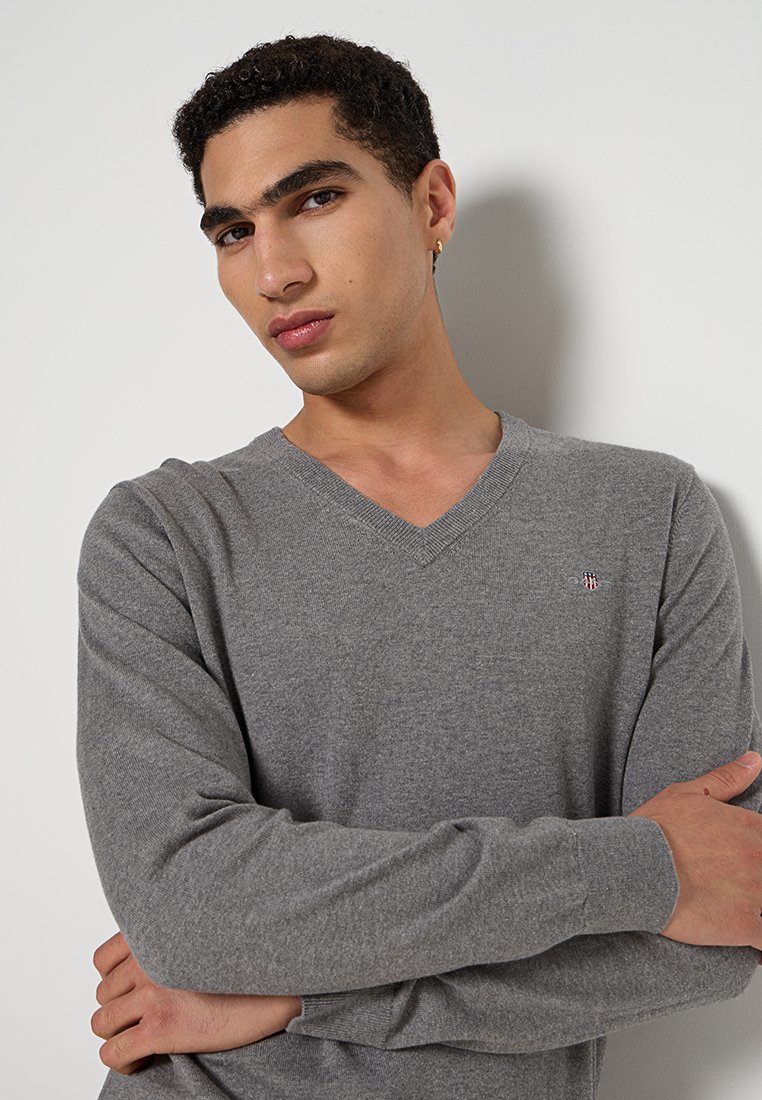 Grau v-förmiger Pullover aus weichem Stoff. Verfügt über lange Ärmel und ein kleines, gesticktes Logo auf der Brust. Glatte Textur und taillierte Form.