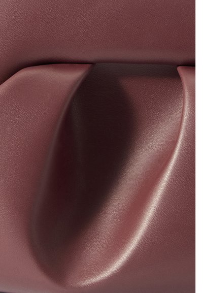 Σκοτεινής μπορντό δερμάτινη επιφάνεια με μια ομαλή, καμπυλωτή εσοχή και διακριτή υφή κάτω από απαλό φωτισμό.