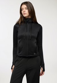 Hoodie corto nero con colletto alto, maniche lunghe, coulisse regolabile e tasche laterali; realizzato in un tessuto liscio e elastico.
