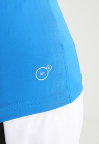 Niebieska koszulka sportowa z teksturowanej tkaniny, z logo "DRY CELL" w białym kolorze. Gładki design z widocznymi szwami po bokach.